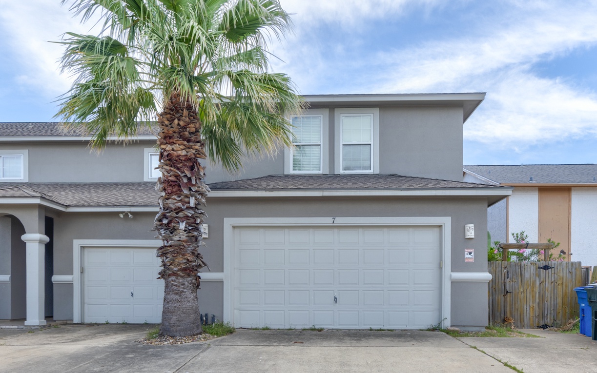 Modern two-story townhome with a private garage and a palm tree, located in a quiet residential neighborhood.