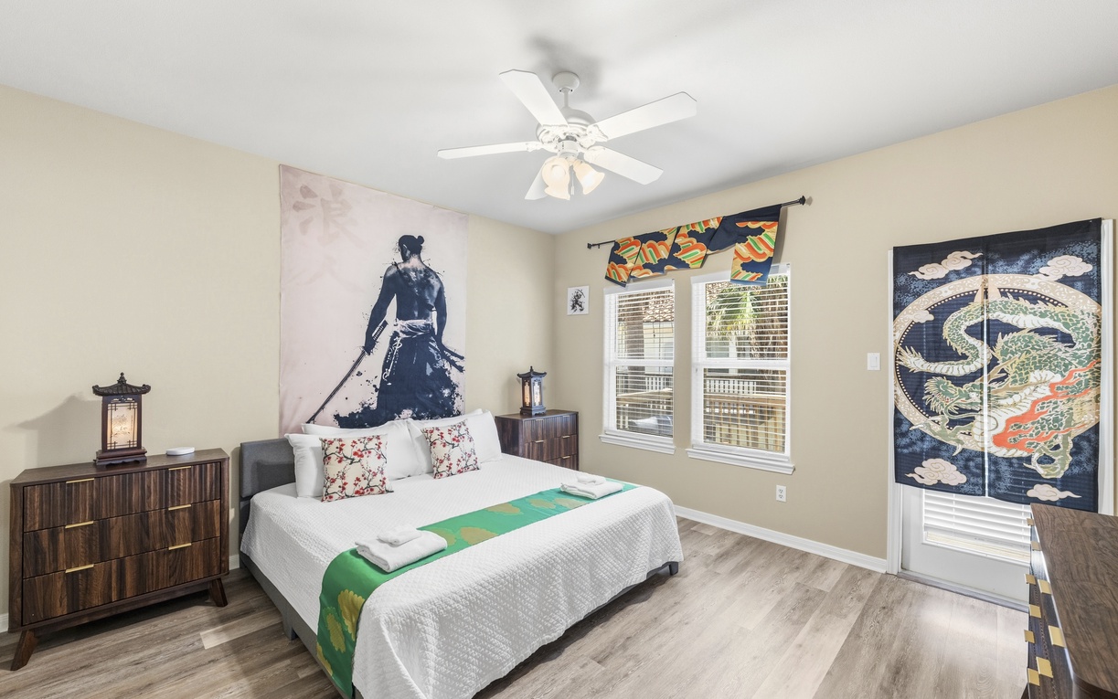 Unwind in your serene bedroom with plush bedding, Asian-inspired decor, and a ceiling fan for comfort. Natural light streams through the windows, while unique artwork creates a calming retreat.