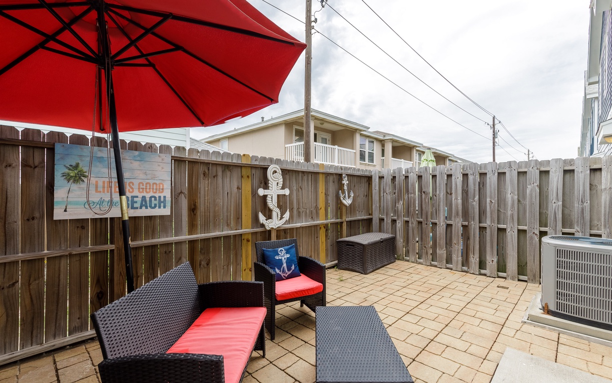 Your private patio offers comfortable seating with vibrant beach-themed decor, perfect for morning coffee or evening relaxation under the red umbrella.