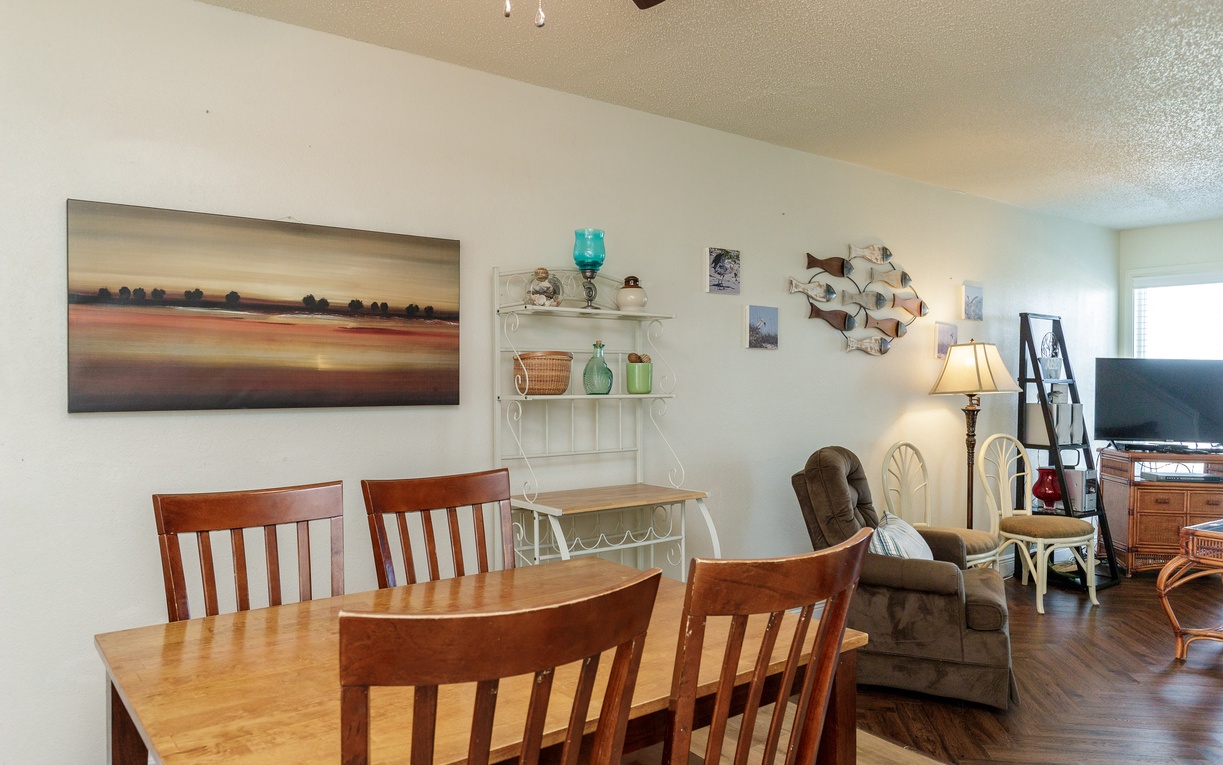 Your open-concept living space combines dining and relaxation, with warm wood furniture and coastal artwork creating a welcoming atmosphere for meals and conversation.