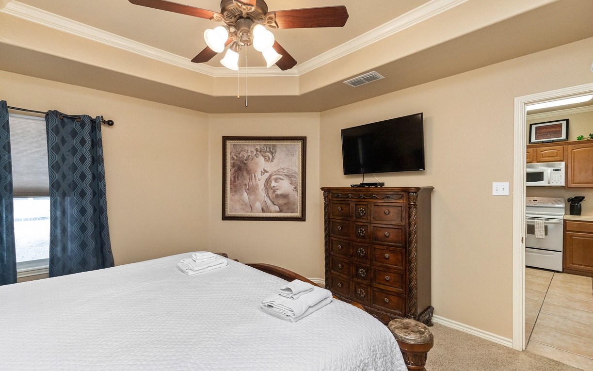 Relax in your comfortable master bedroom with elegant furnishings, ceiling fan, and flat-screen TV for perfect comfort.