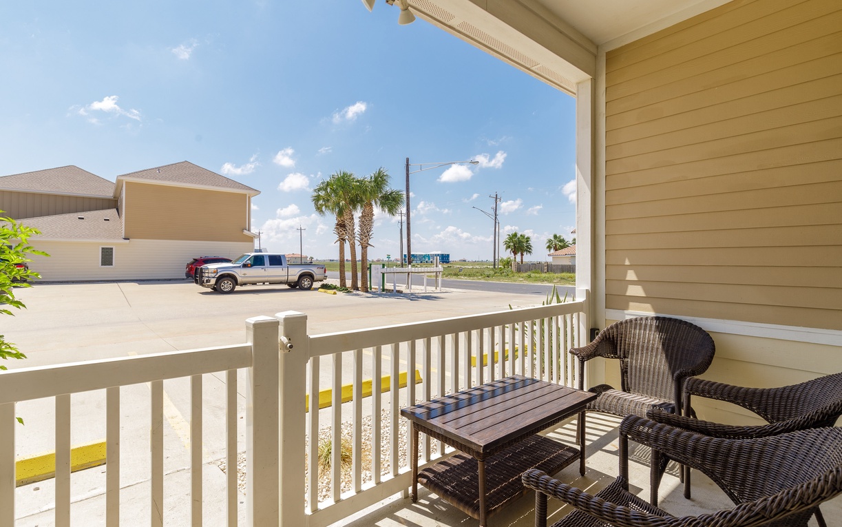 Relax on your private balcony with comfortable wicker seating while enjoying the sunny coastal atmosphere and peaceful neighborhood views.