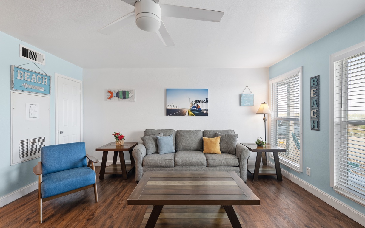 Relax in your coastal-inspired living room with soft breezes from the ceiling fan, bright natural light, and comfy seating. The beach-themed decor and soothing blue tones set the perfect tone for your stay.