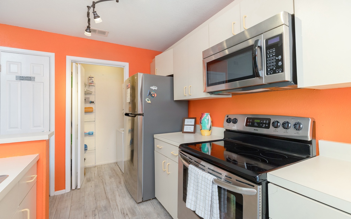 Bright orange walls energize your fully-equipped kitchen, featuring stainless steel appliances and everything needed for home-cooked meals.