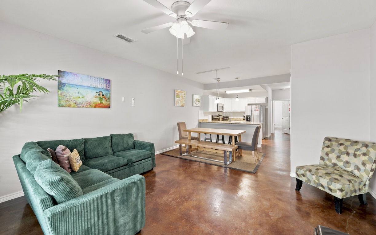 Settle into your spacious open-concept living area where a plush green sectional and stylish dining space invite you to relax and connect. Gleaming polished floors catch the light while your modern kitchen awaits just steps away.