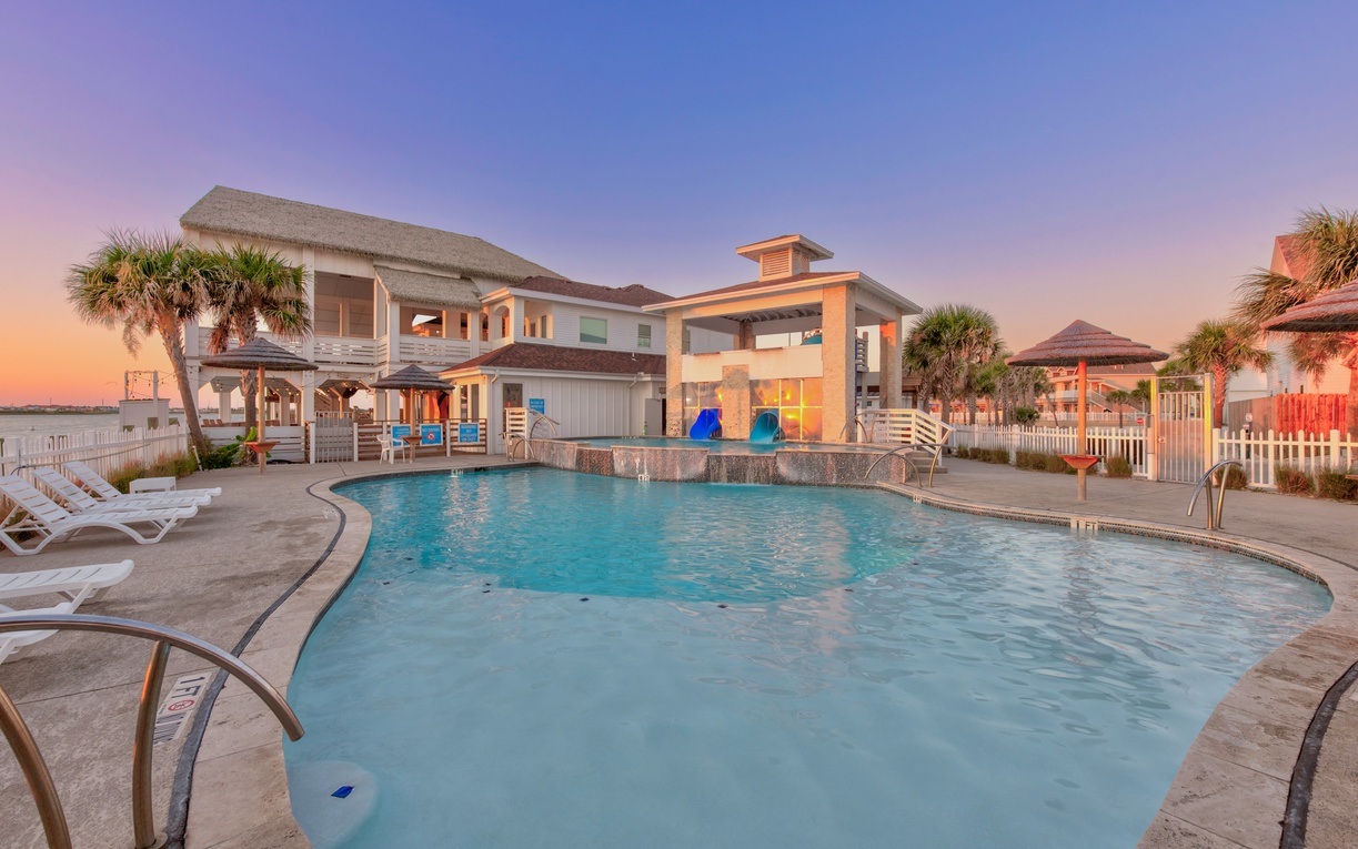 Modern beachfront property featuring a pristine swimming pool area surrounded by tropical palm trees and contemporary architecture during golden hour.