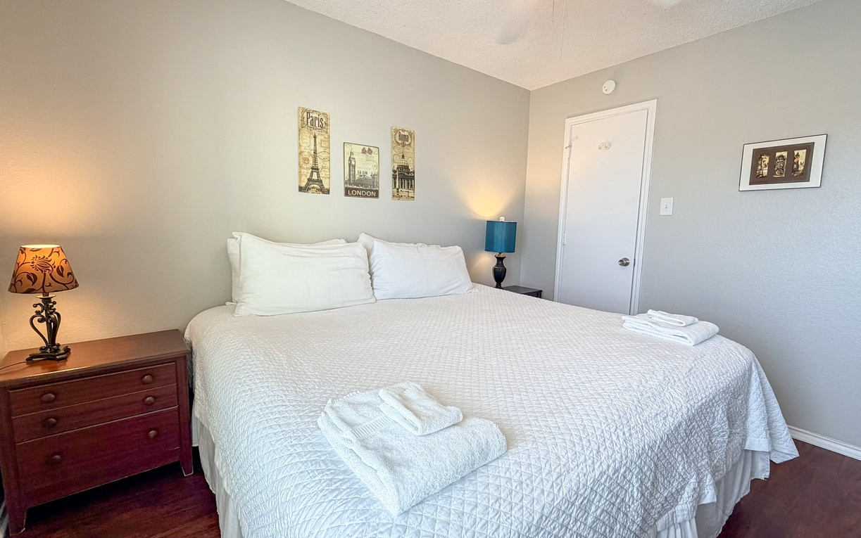 Sink into crisp white linens in your peaceful bedroom, where soft lighting and travel-inspired art create the perfect retreat for restful nights.
