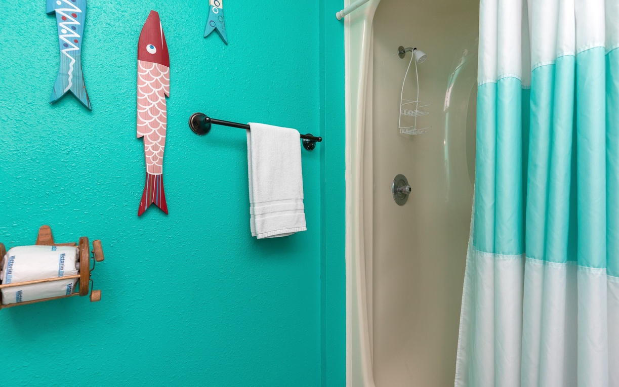 Step into your vibrant beach-themed bathroom where turquoise walls and playful fish décor create a coastal retreat for refreshing showers.