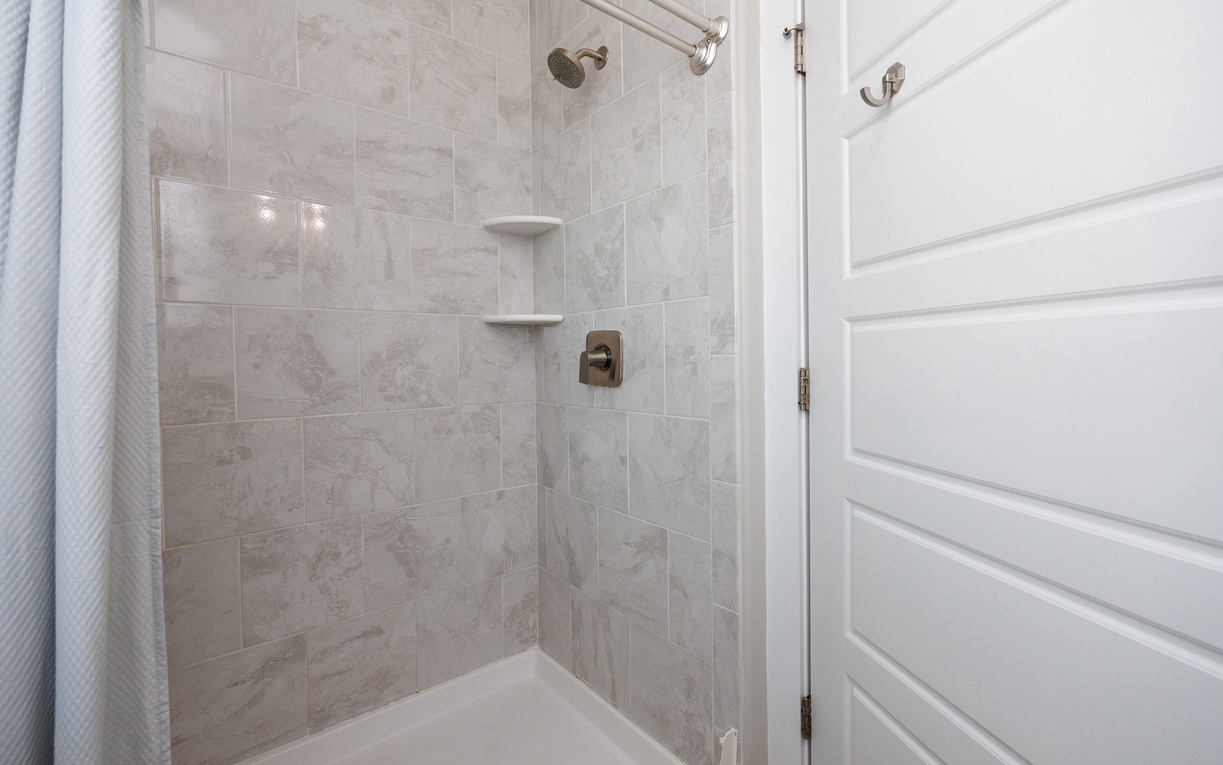 Refresh in your elegantly tiled shower featuring modern fixtures, built-in shelving, and sleek marble-look walls for a spa-like experience.