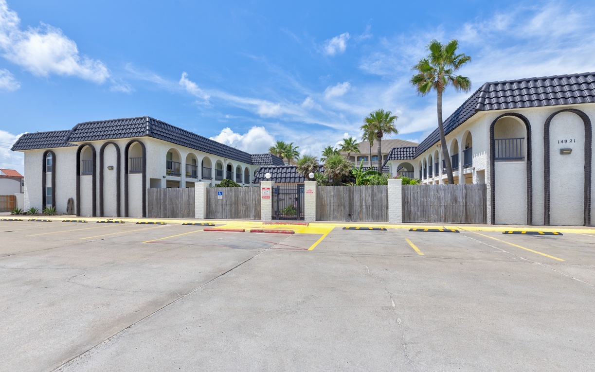 Mediterranean-style property complex with palm trees and convenient parking area under sunny blue skies.