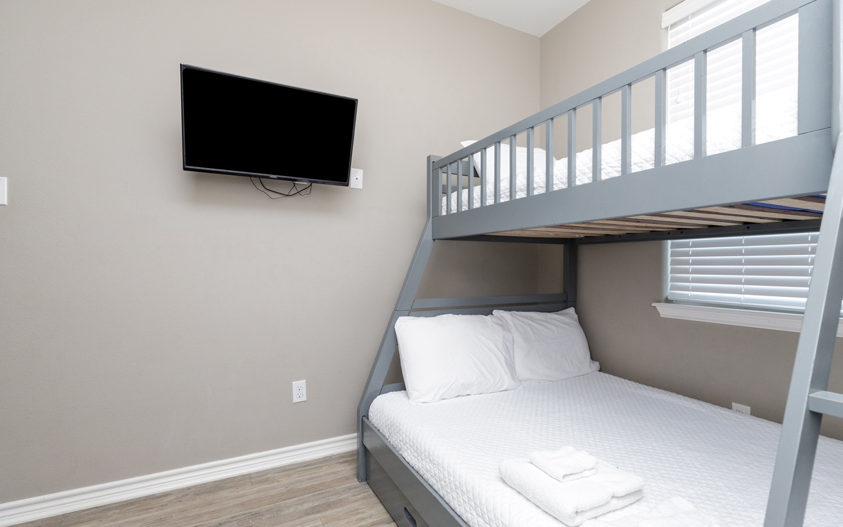 Cozy bunk bed room with wall-mounted TV perfect for families. Crisp white linens await your arrival in this comfortable sleeping space.