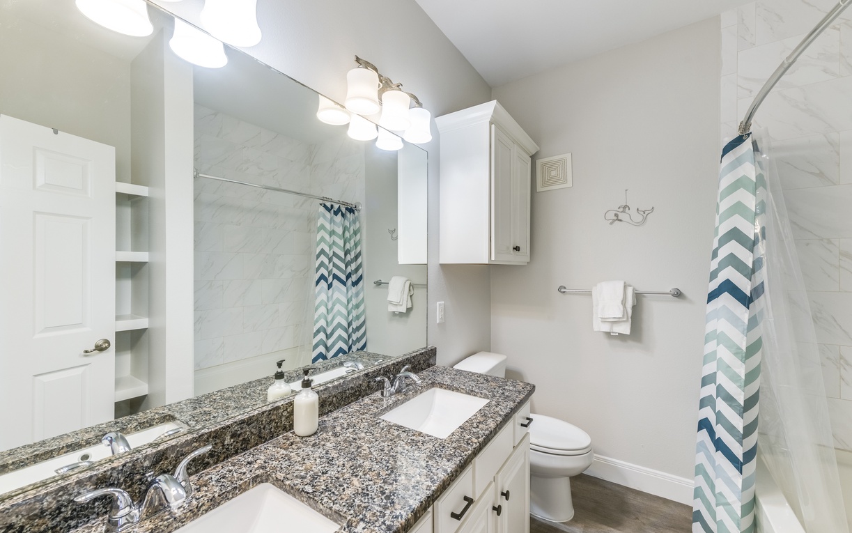 Step into your spotless bathroom featuring granite countertops, dual sinks, and a refreshing tub-shower combo with cheerful chevron accents.
