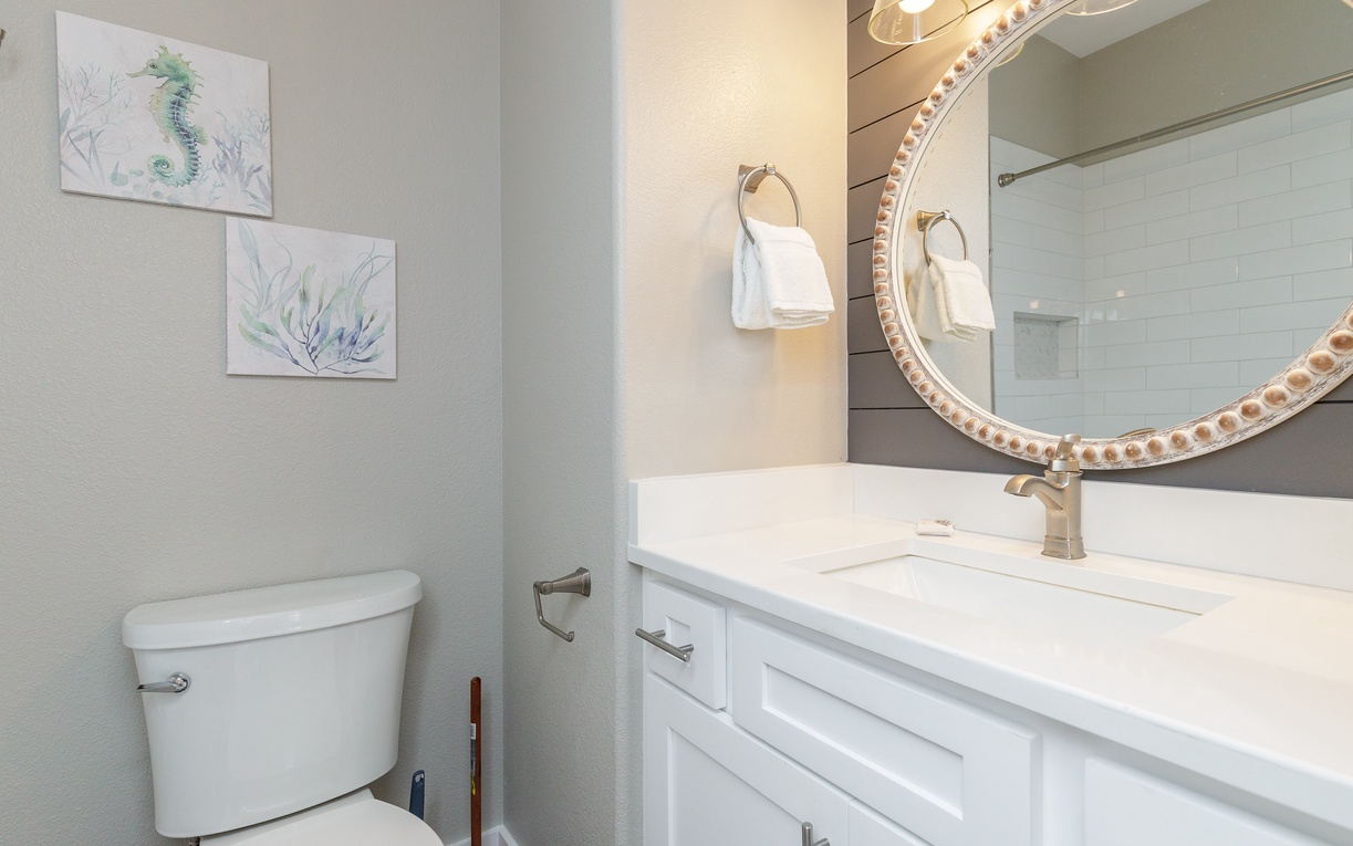 Freshen up in your elegant guest bathroom featuring soft coastal artwork and pristine marble finishes for a peaceful start to your day.