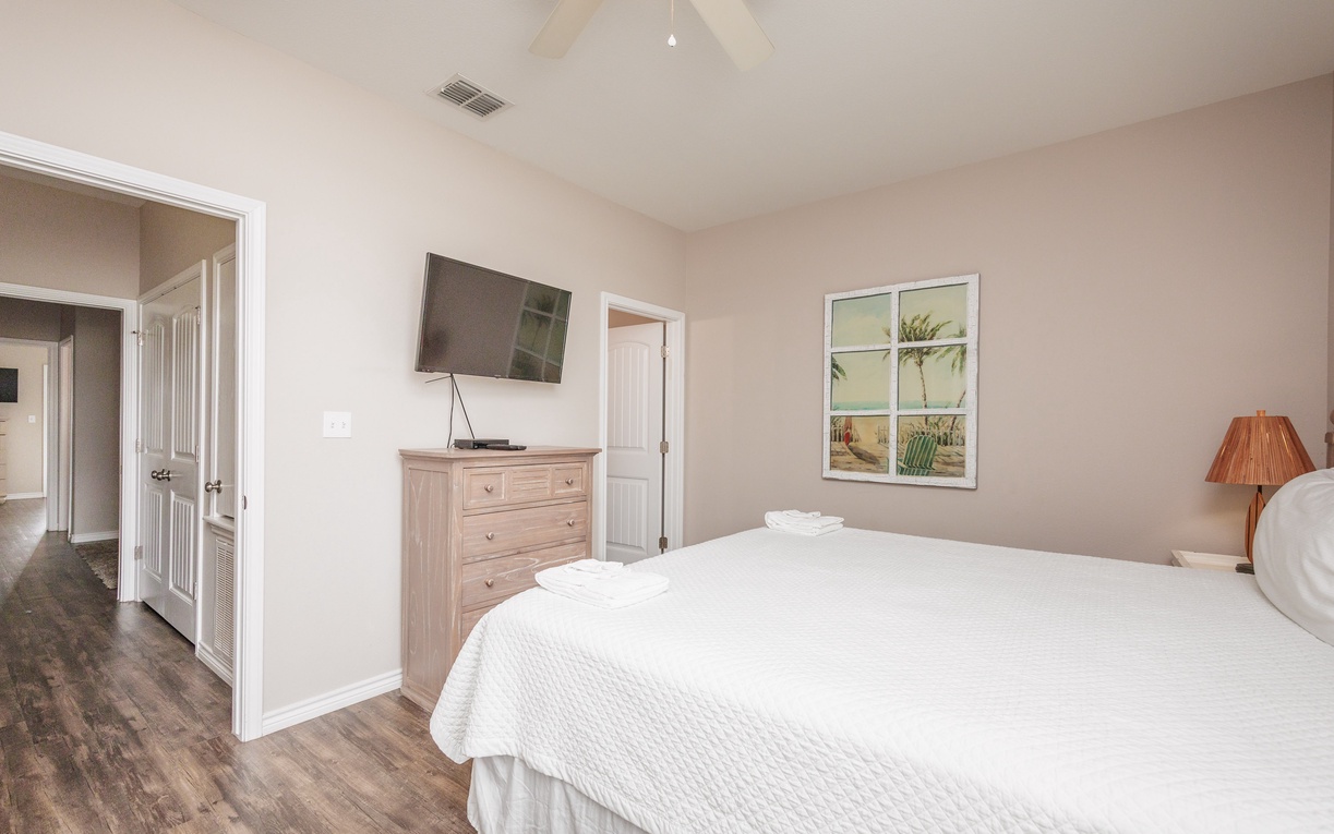Unwind in your peaceful bedroom featuring crisp linens, beachy coastal art, and a wall-mounted TV for your evening entertainment.
