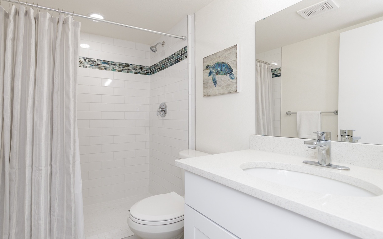 Refresh in your pristine bathroom featuring a luxurious tub-shower combo, crisp white finishes, and charming sea turtle artwork that adds coastal character.