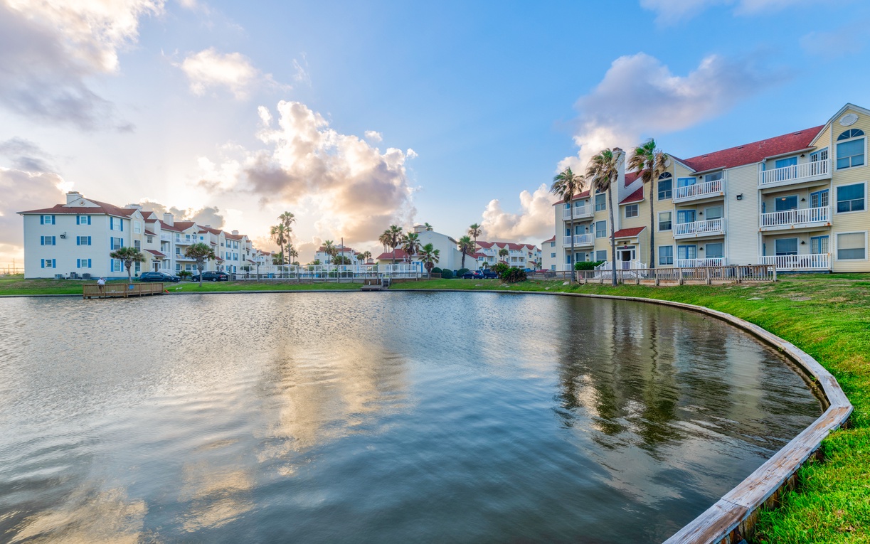Waterfront vacation rental community featuring colorful buildings surrounding a peaceful lagoon with palm trees and dramatic sky.