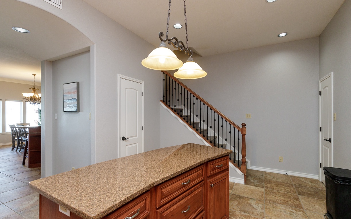 Your spacious kitchen island awaits with granite countertops and warm wood cabinets, perfectly positioned beneath elegant pendant lighting for memorable meal prep.