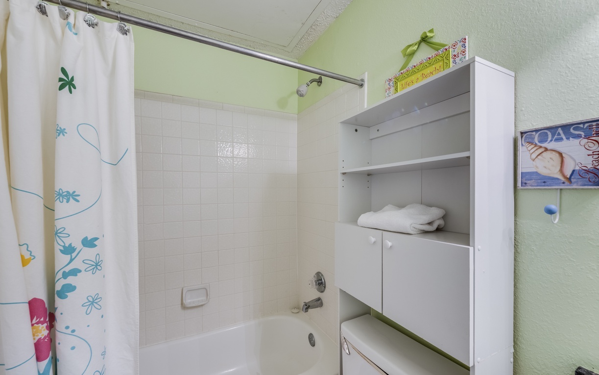 Full guest bathroom featuring a tub/shower combination and built-in shelving stocked with fresh towels and essentials.