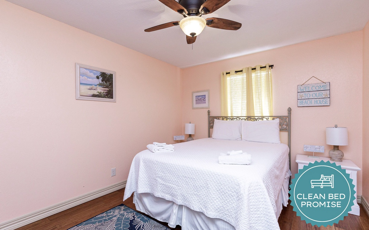 Sink into your coastal sanctuary with crisp linens, gentle ceiling fan breeze, and charming beach artwork welcoming you home.
