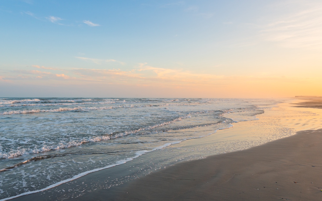 Pristine sandy beach meets rolling ocean waves under a golden sunset sky, creating the perfect coastal retreat setting.