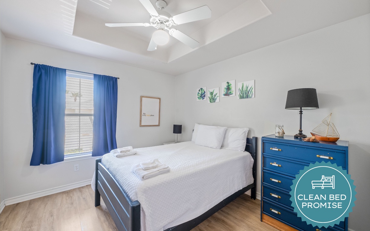 Drift off in this tranquil bedroom featuring fresh linens, coastal decor, and a ceiling fan for your perfect night's sleep.