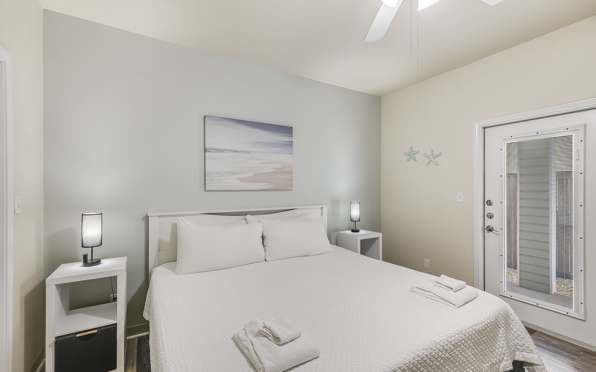 Your peaceful bedroom features a comfortable bed with fresh linens and towels, calming coastal artwork, and private patio access.