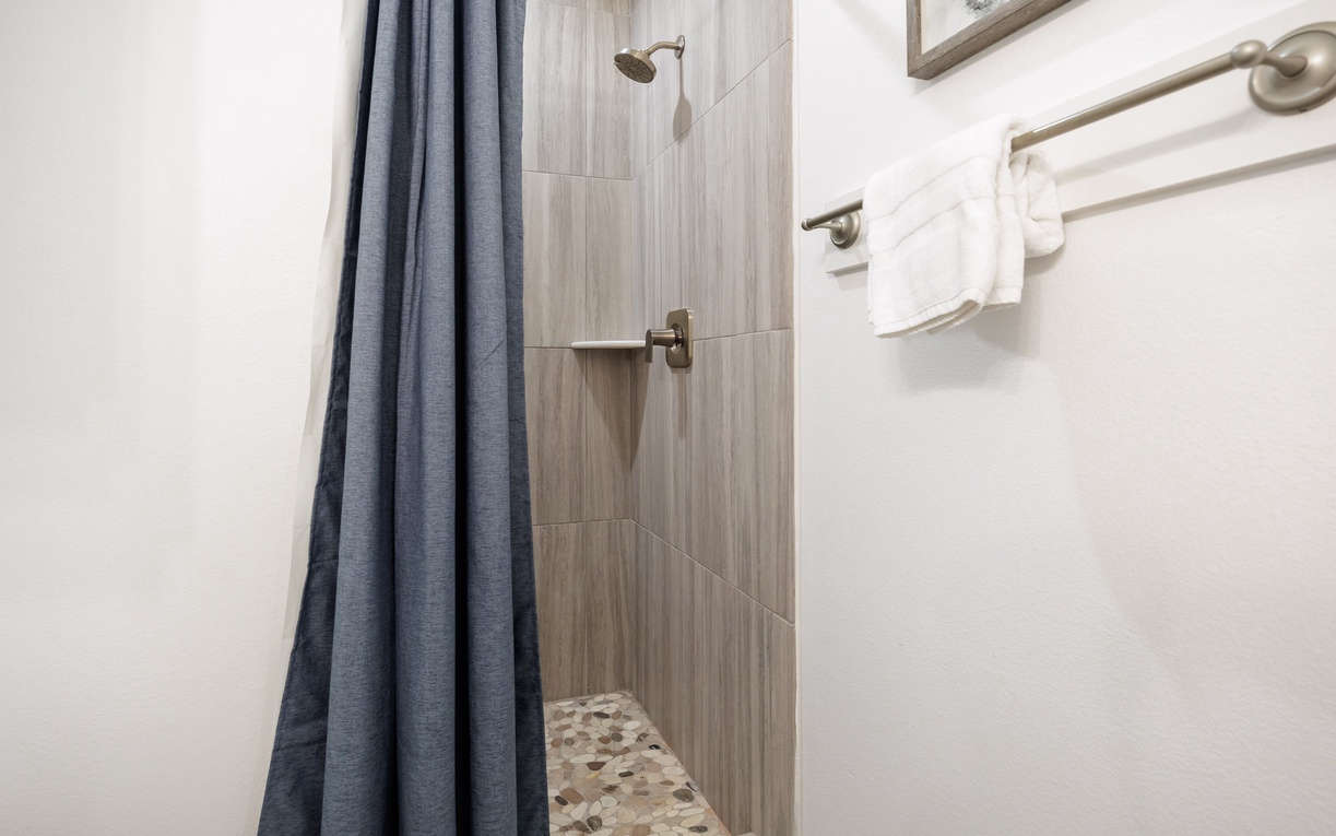 Step into your private shower sanctuary with sleek wood-grain tiles and rainfall showerhead, where fluffy towels await your refreshing morning routine.