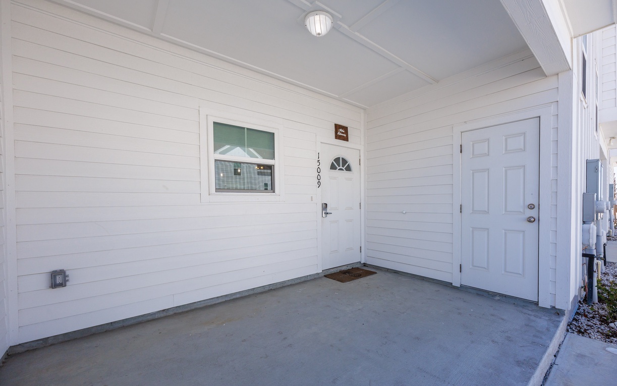 Clean, covered entrance with white siding and well-lit access to unit 100.