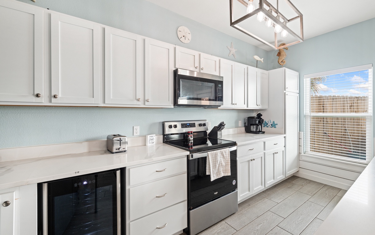 Step into your bright, coastal-inspired kitchen with crisp white cabinetry, modern appliances, and soft blue walls. Enjoy morning coffee while glimpsing the palms swaying outside your window.