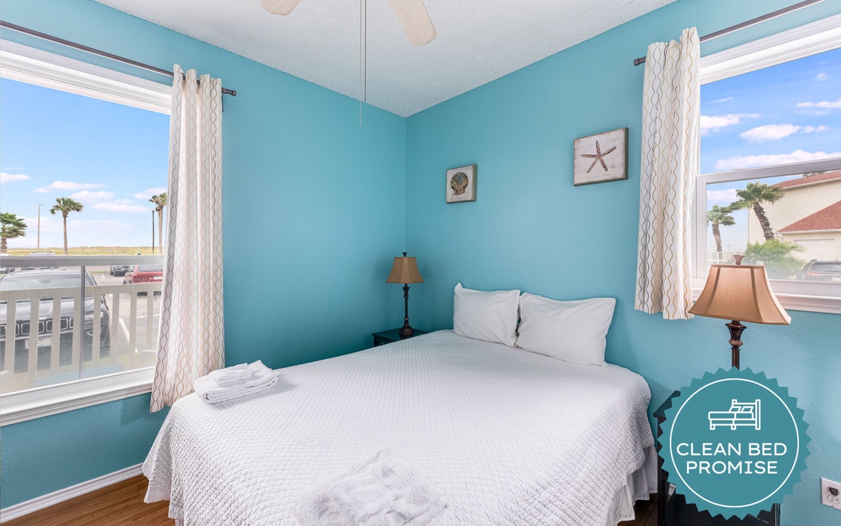 Wake up in this ocean-inspired bedroom with coastal views through dual windows, crisp white linens, and soothing turquoise walls that bring beachside serenity indoors.