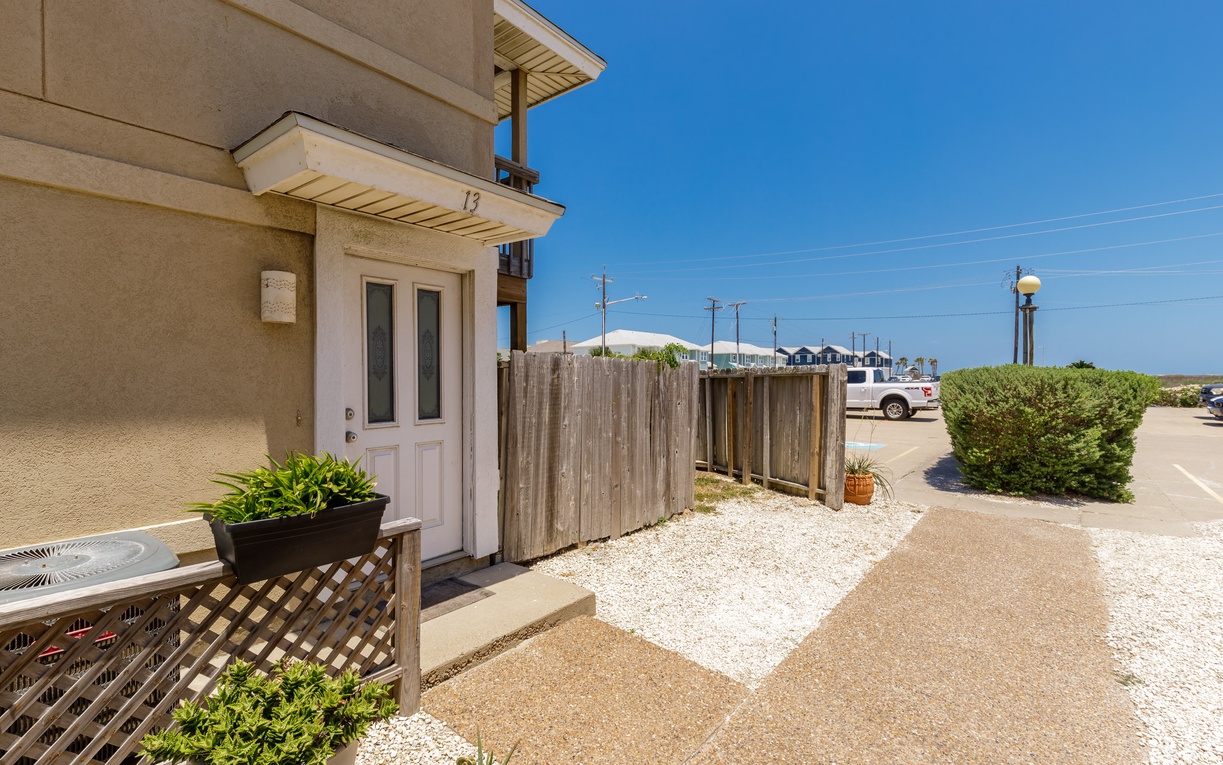 This beachside property entrance offers convenient parking and a welcoming entry with mature landscaping in a quiet coastal setting.