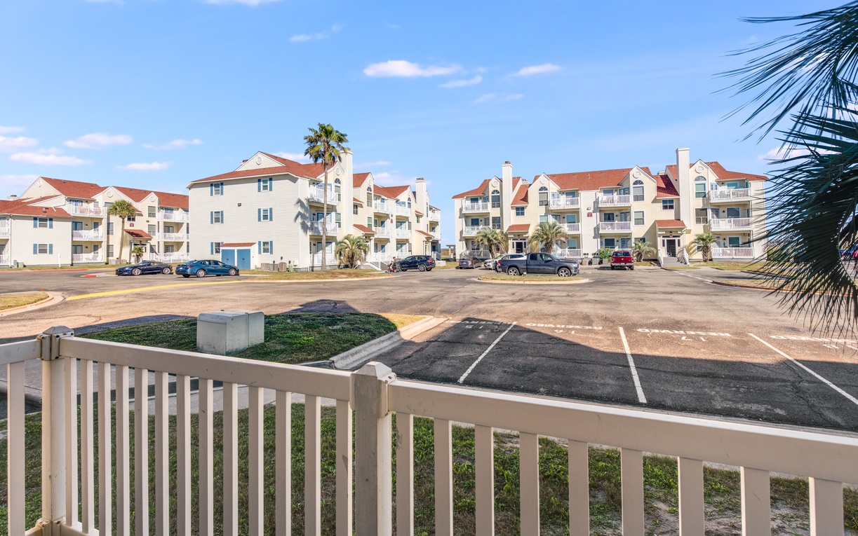 Beachside resort community with multi-level buildings, red tile roofs, and tropical palm trees under blue skies.