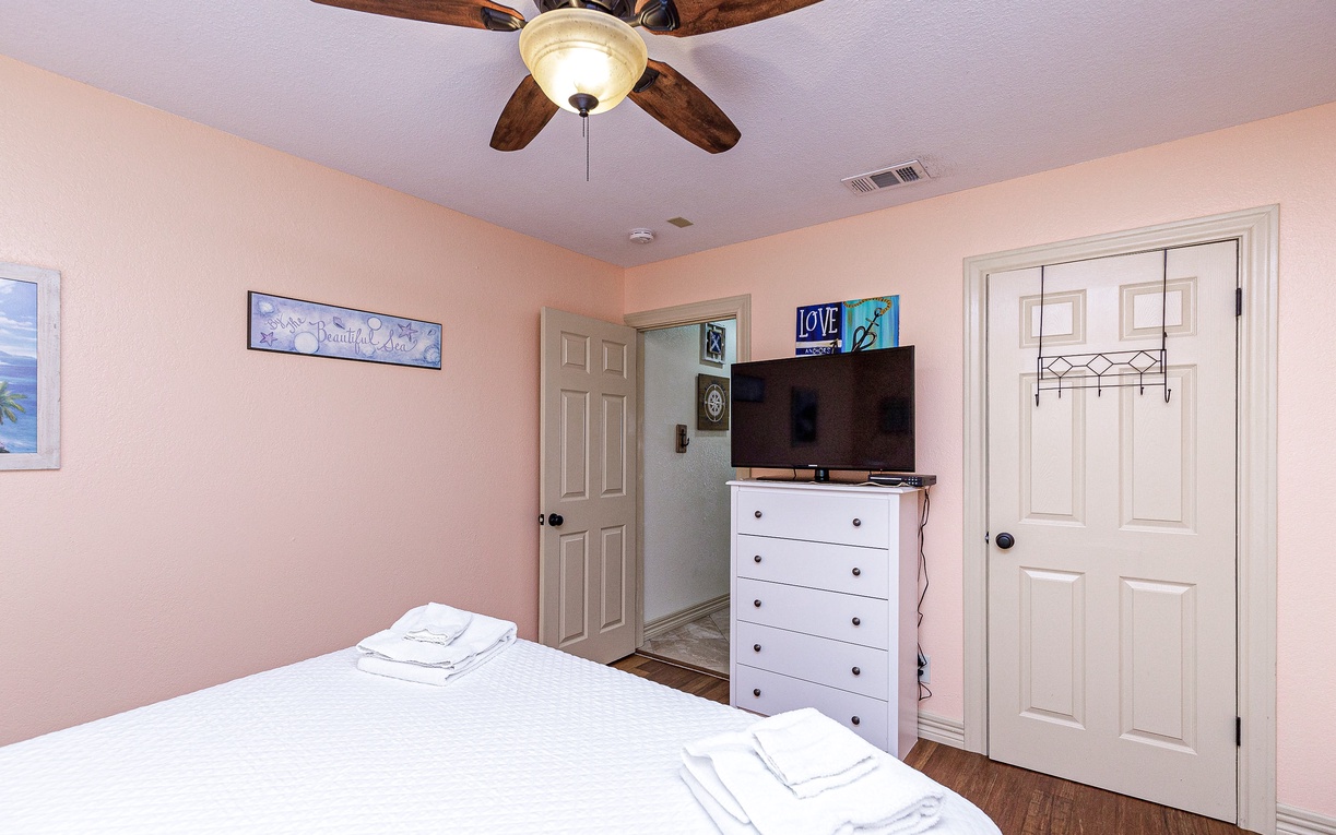 Your comfortable bedroom features soft pink walls, ceiling fan, flat-screen TV, and plenty of storage space for a restful stay.