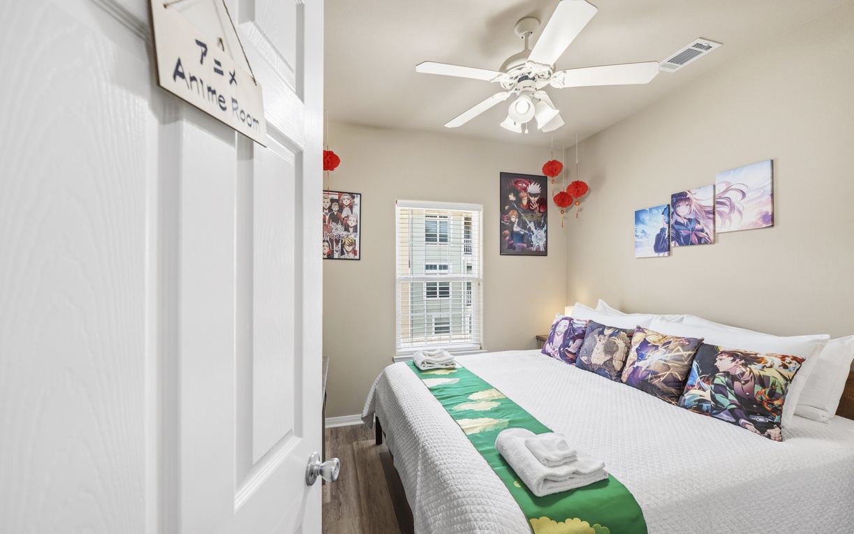 Step into your anime-inspired bedroom where vibrant artwork and cozy linens await. Fresh towels and a plush bed invite you to unwind in style beneath a gentle ceiling fan.