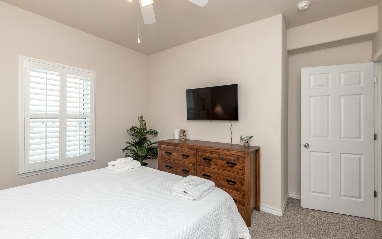 Unwind in your tranquil bedroom featuring crisp white linens, warm wood furnishings, and natural light streaming through plantation shutters.