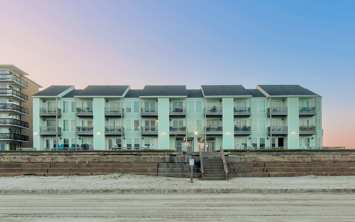 Beachfront property featuring multiple balconied units with direct beach access via stone steps and seawall walkway.