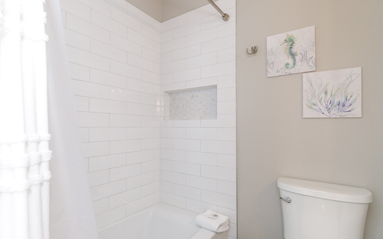 Step into your pristine bathroom where coastal artwork adds charm to the crisp white subway tile shower.