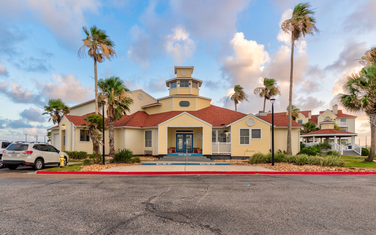 Coastal vacation rental with distinctive yellow exterior and red tile roof, surrounded by swaying palm trees in a tropical setting.