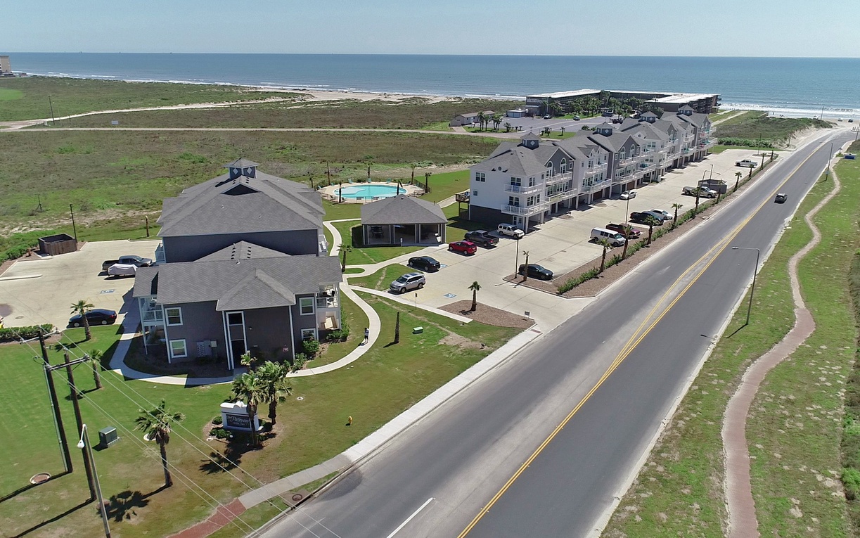 Aerial view of beachfront vacation rental development featuring multiple accommodations and swimming pool, positioned between coastal road and ocean shoreline.