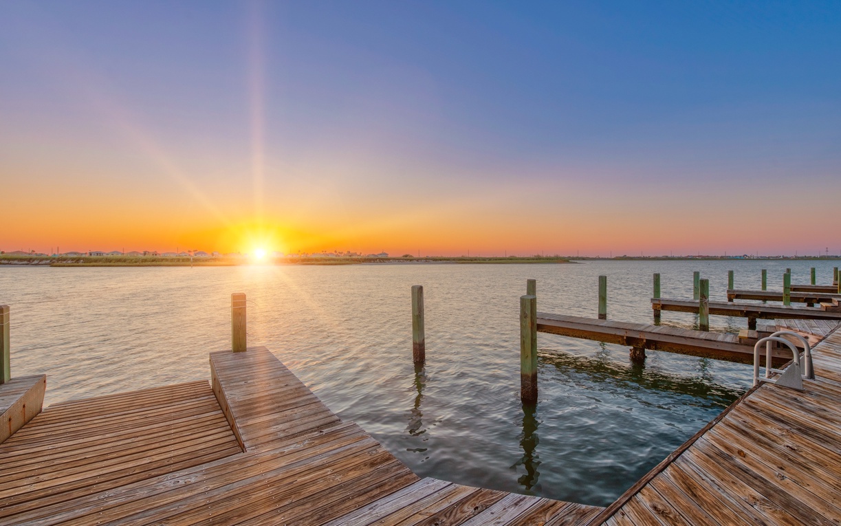 Stunning waterfront sunset paints the sky in golden hues over peaceful waters and wooden marina docks.