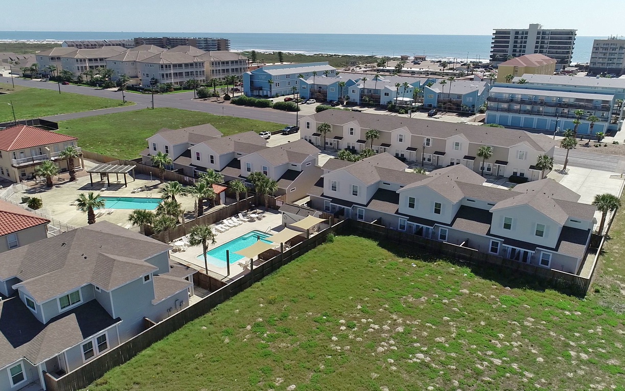 Aerial view of beachside vacation rental community with pools, palm trees, and ocean proximity in a peaceful coastal setting.