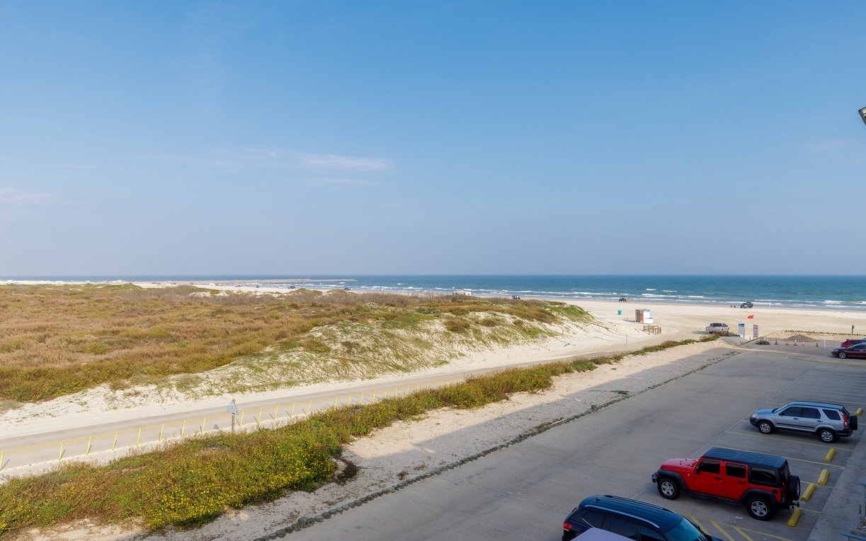 Pristine coastal beach with natural dunes and convenient parking area under clear blue skies.