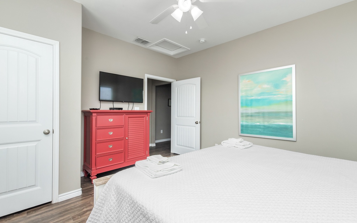 Your peaceful bedroom features crisp linens, coral accent dresser, flat-screen TV, and soothing coastal artwork for ultimate relaxation.