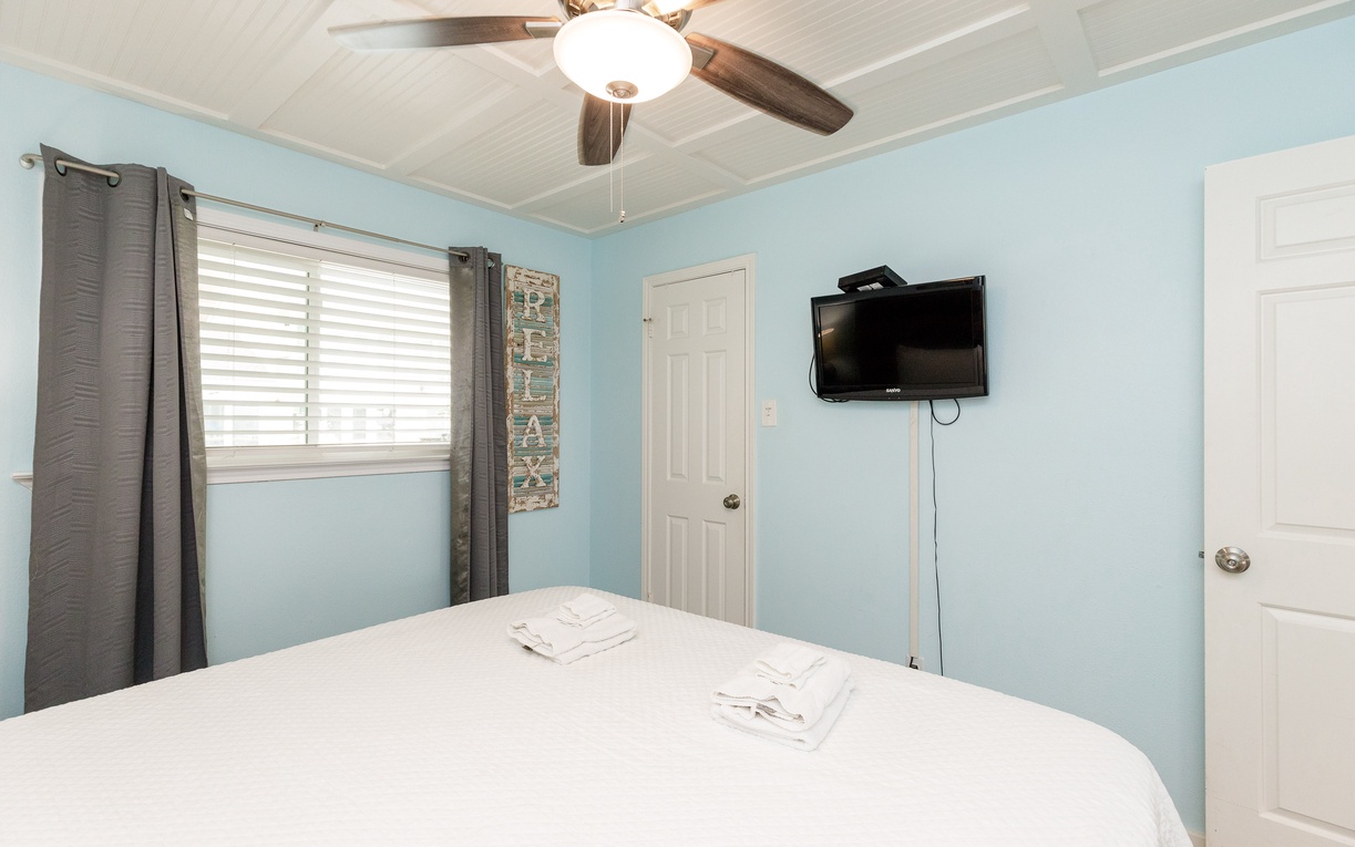 Drift off in your serene bedroom with soft blue walls, a ceiling fan for comfort, and entertainment ready at your fingertips.