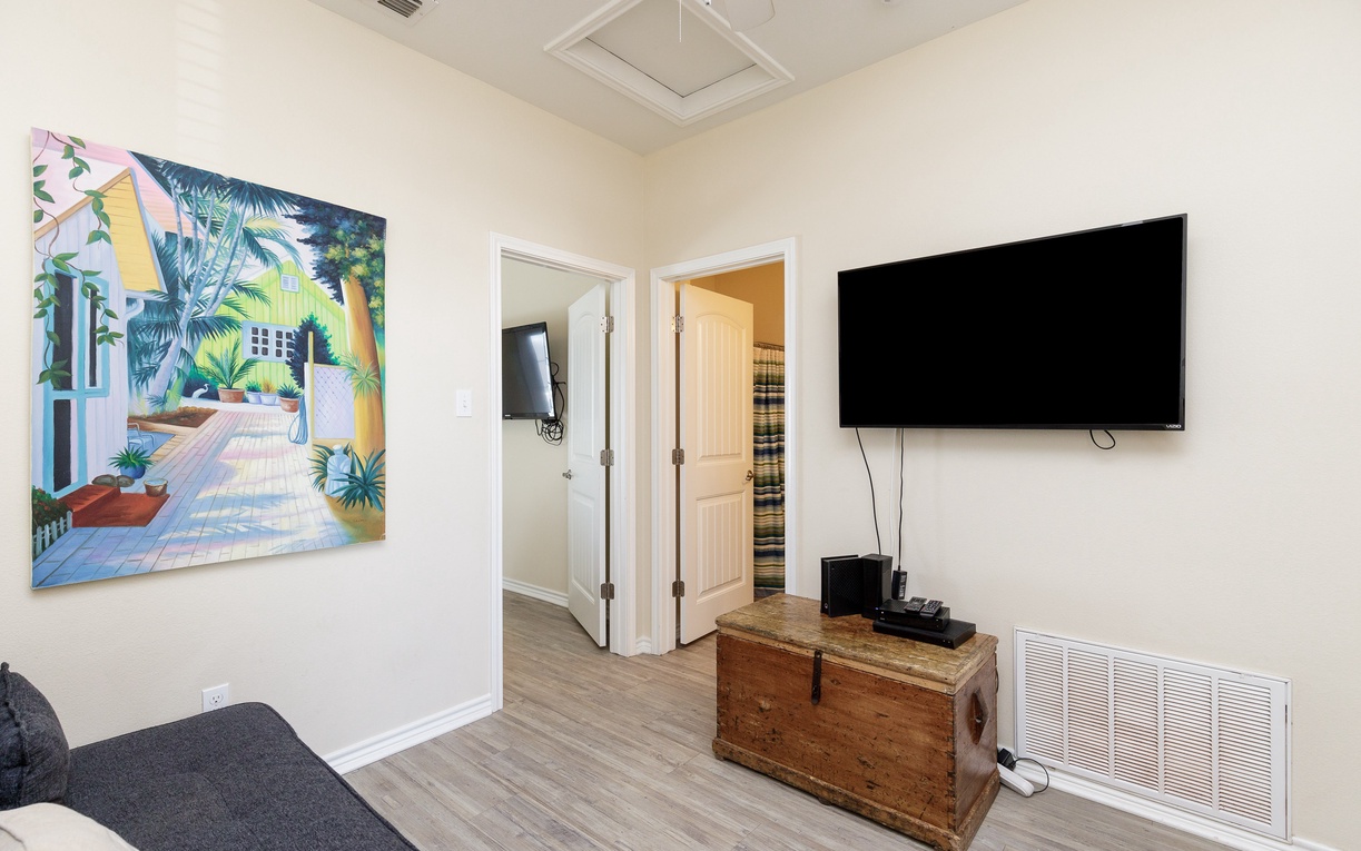Unwind in your bright living space featuring a large wall-mounted TV and tropical artwork creating a cheerful, relaxing atmosphere.