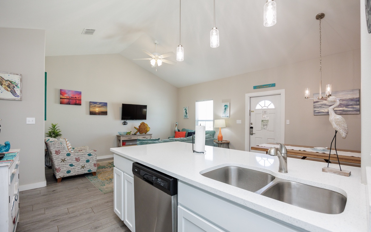 Your open-concept kitchen flows seamlessly into the living room, featuring modern appliances and coastal artwork that creates a welcoming space for cooking and relaxing.