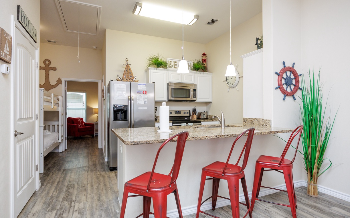 Your fully equipped kitchen features granite counters and cheerful red stools where you can enjoy morning coffee or plan your beach adventures.