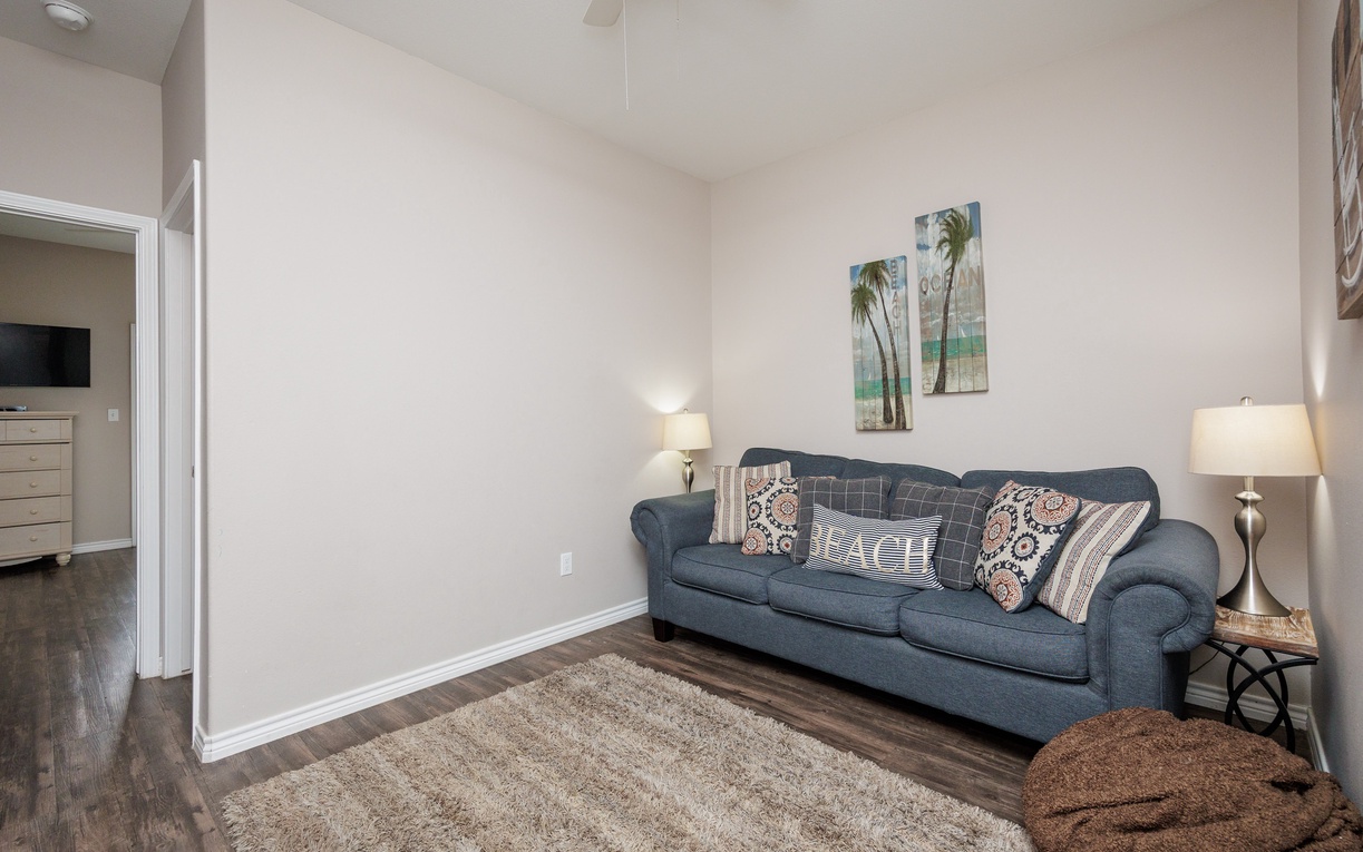 Unwind on your plush sofa in this bright living space, where coastal artwork and soft lighting create the perfect atmosphere for relaxation.