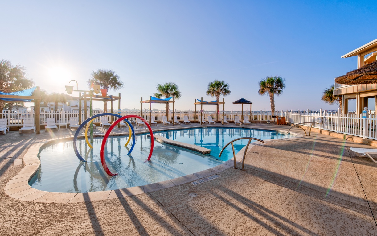 Waterfront pool area with colorful play features and palm trees, perfect for family fun in the coastal sunshine.