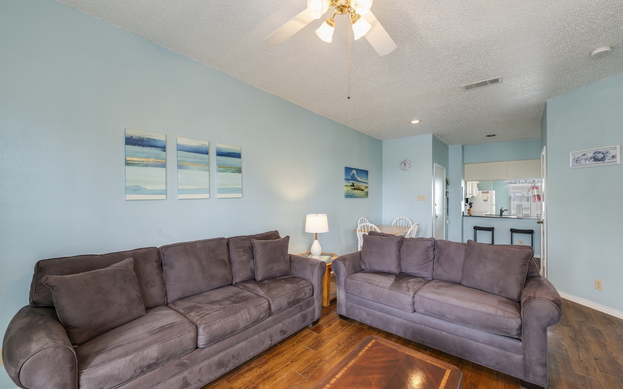 Bright, open living room with comfortable seating, coastal décor, and warm wood floors—perfect for relaxing together after a day at the beach.